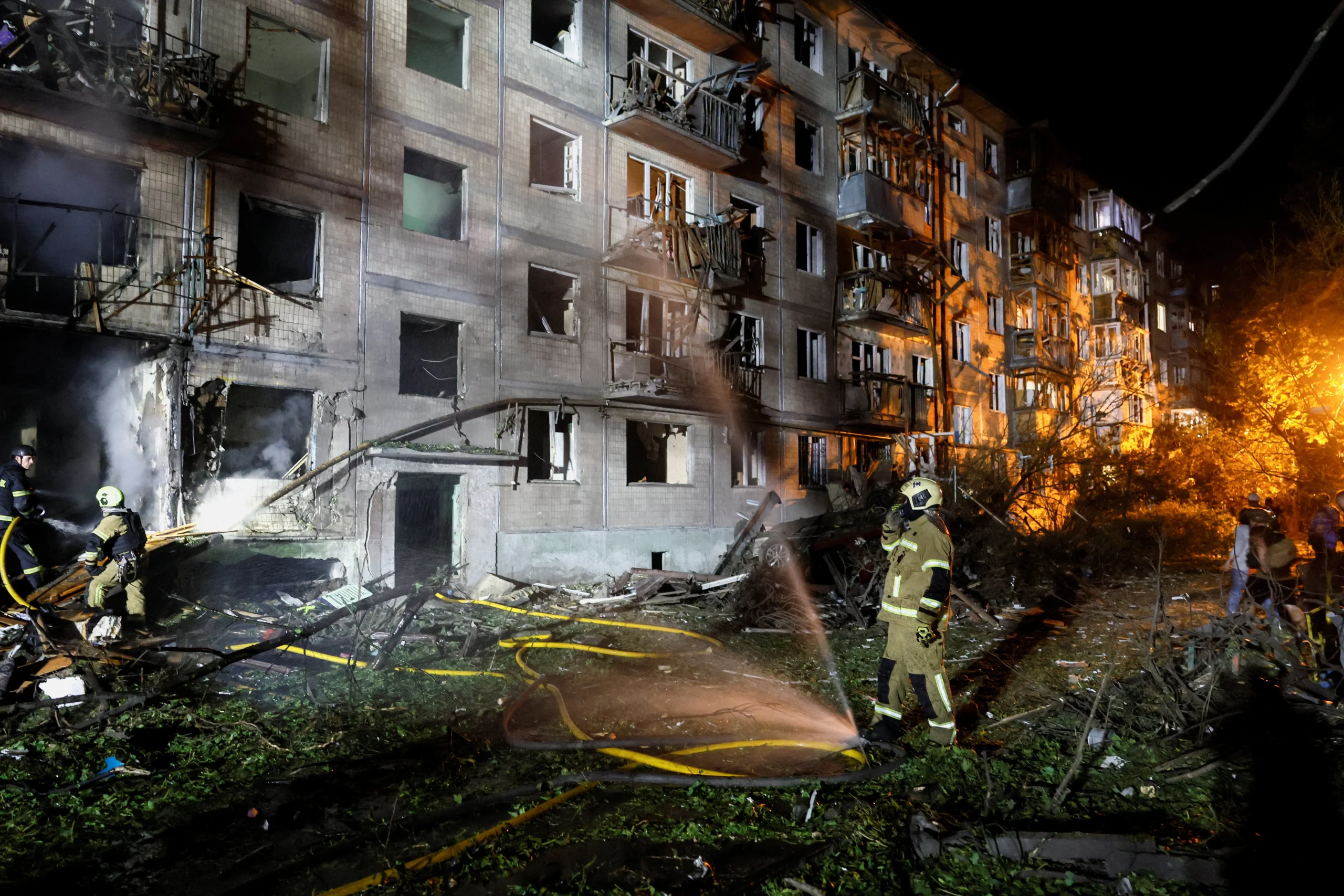 Пожежники гасять пожежу біля зруйнованого багатоповерхівки вночі серед уламків